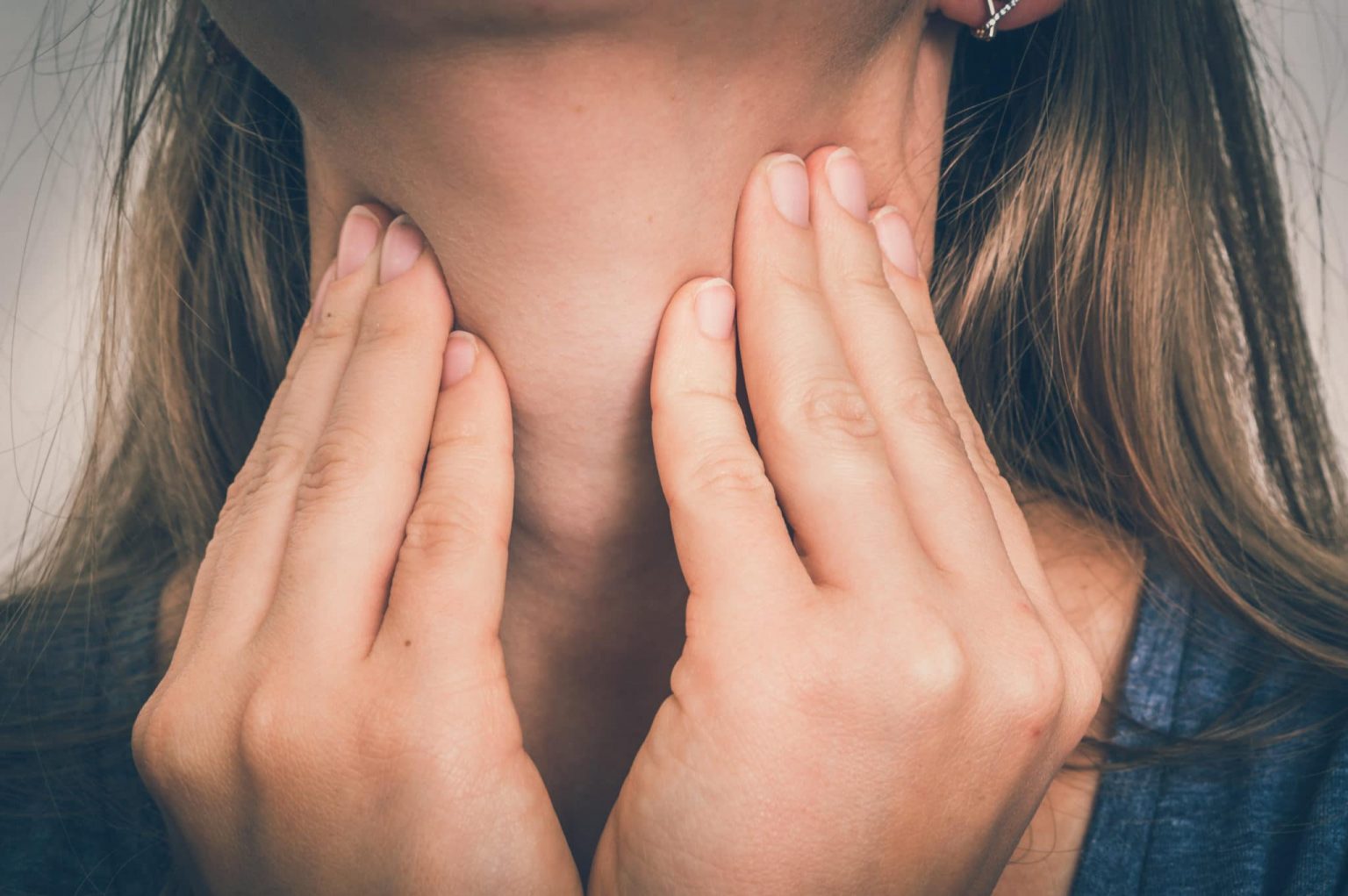Sore-Throat-symptoms Close up of a woman with her finger tips on her neck checking her sore throat.