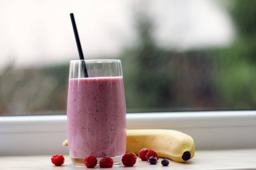 A sensible berry smoothie glass next to a banana.