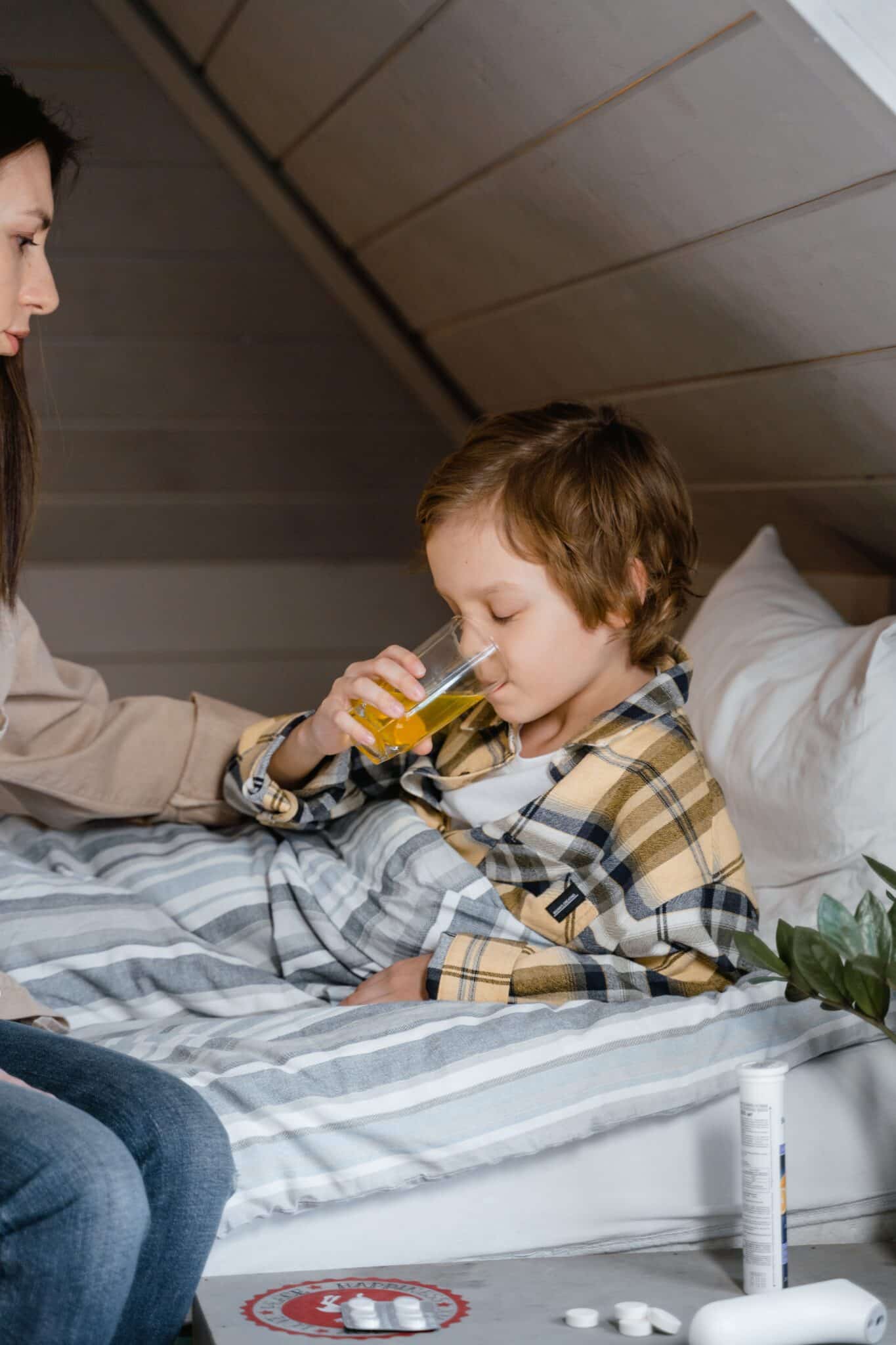 Little boy home sick and resting in bed taking a sip of water.