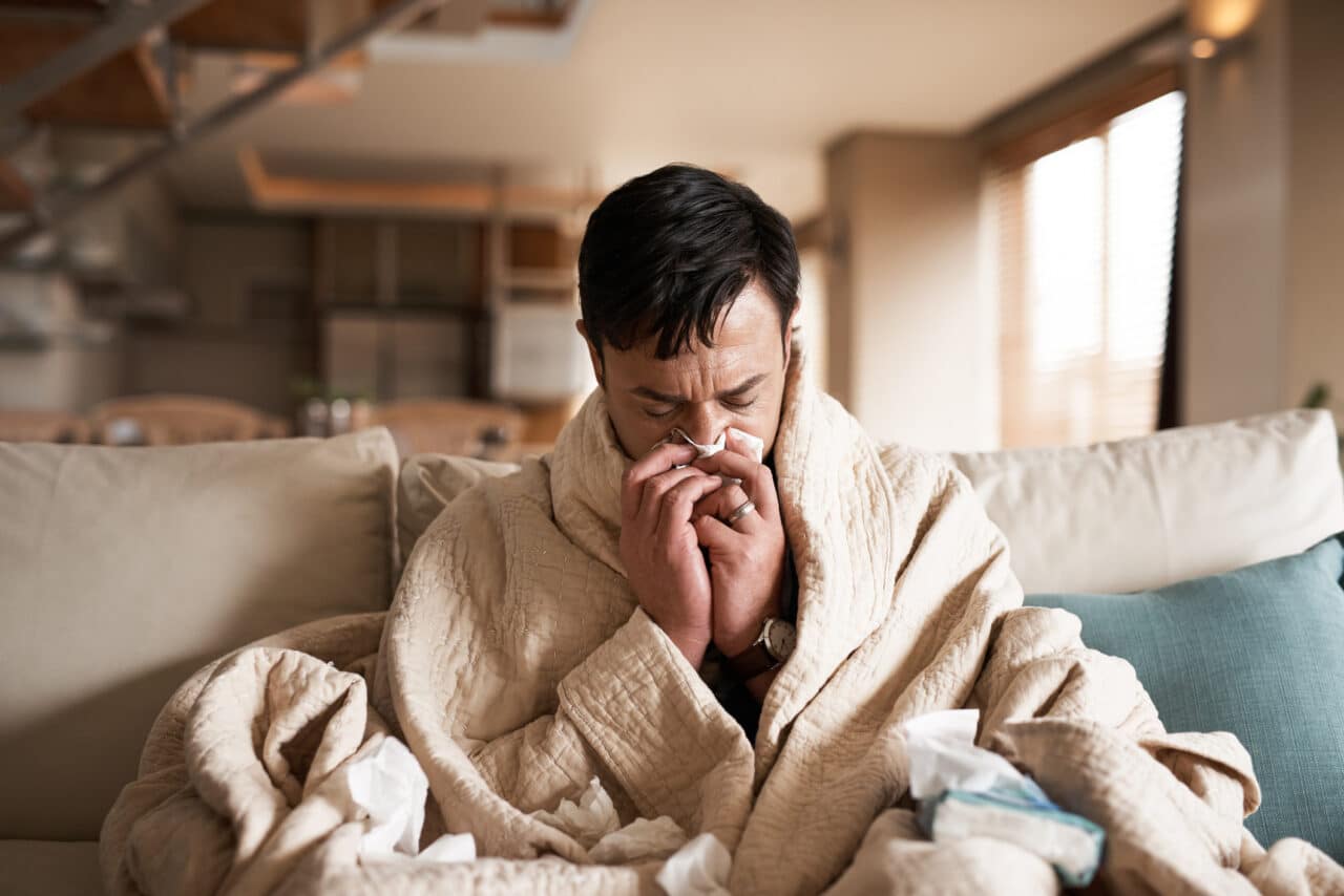 Man sick with a cold blowing his nose on the couch.