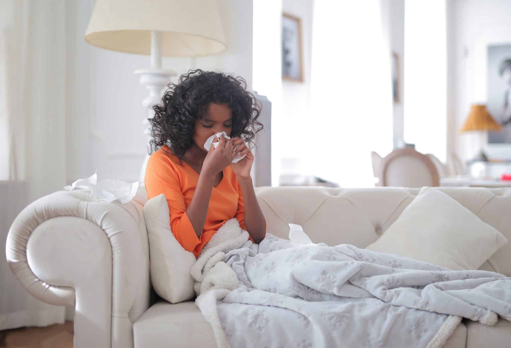 Woman on the couch dealing with a cold and stuffy nose.