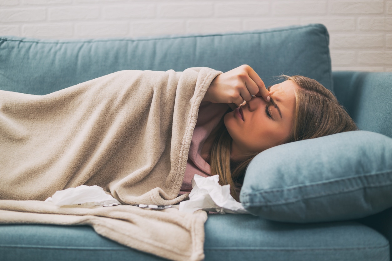 Woman with headache laying on the couch with tissues holding sinuses. 