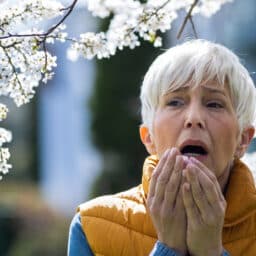 Woman sneezing in the park from allergies