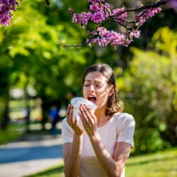 Woman sneezing into a tissue at the park