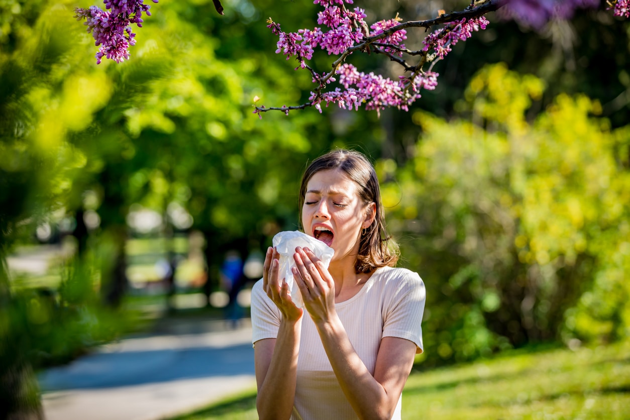 Woman sneezing into a tissue at the park