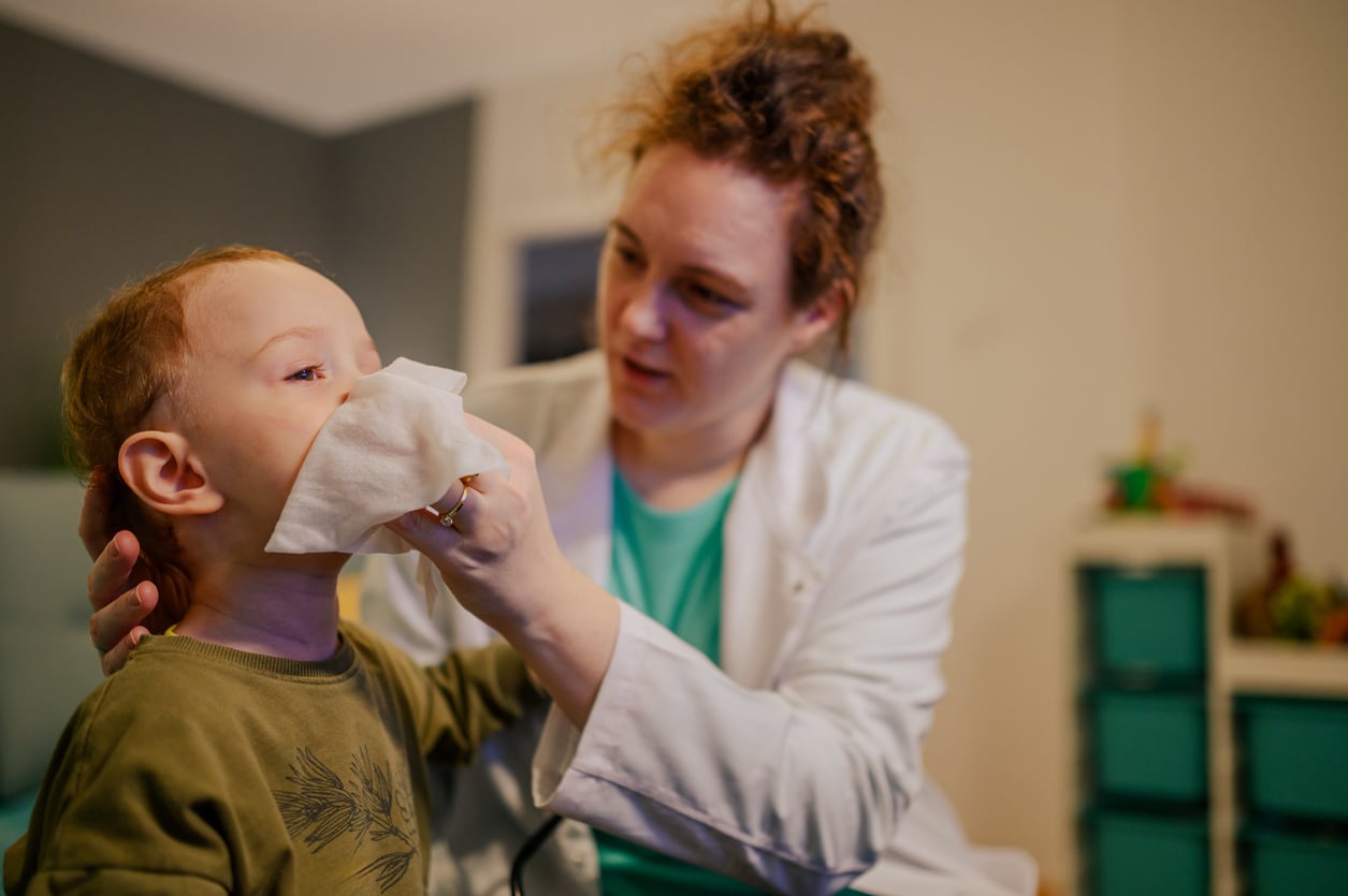 Pediatrician holding a tissue to a young boy's nose.