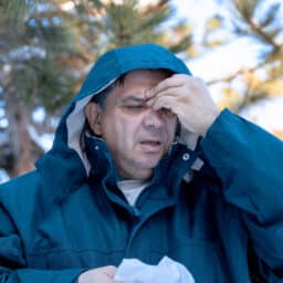 Man with a sinus headache holding his forehead wearing a raincoat.