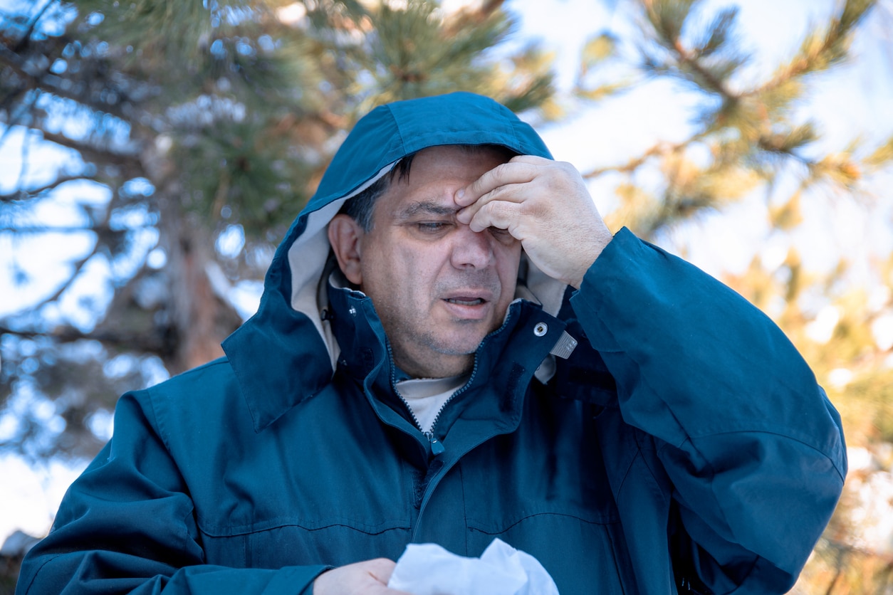 Man with a sinus headache holding his forehead wearing a raincoat. 