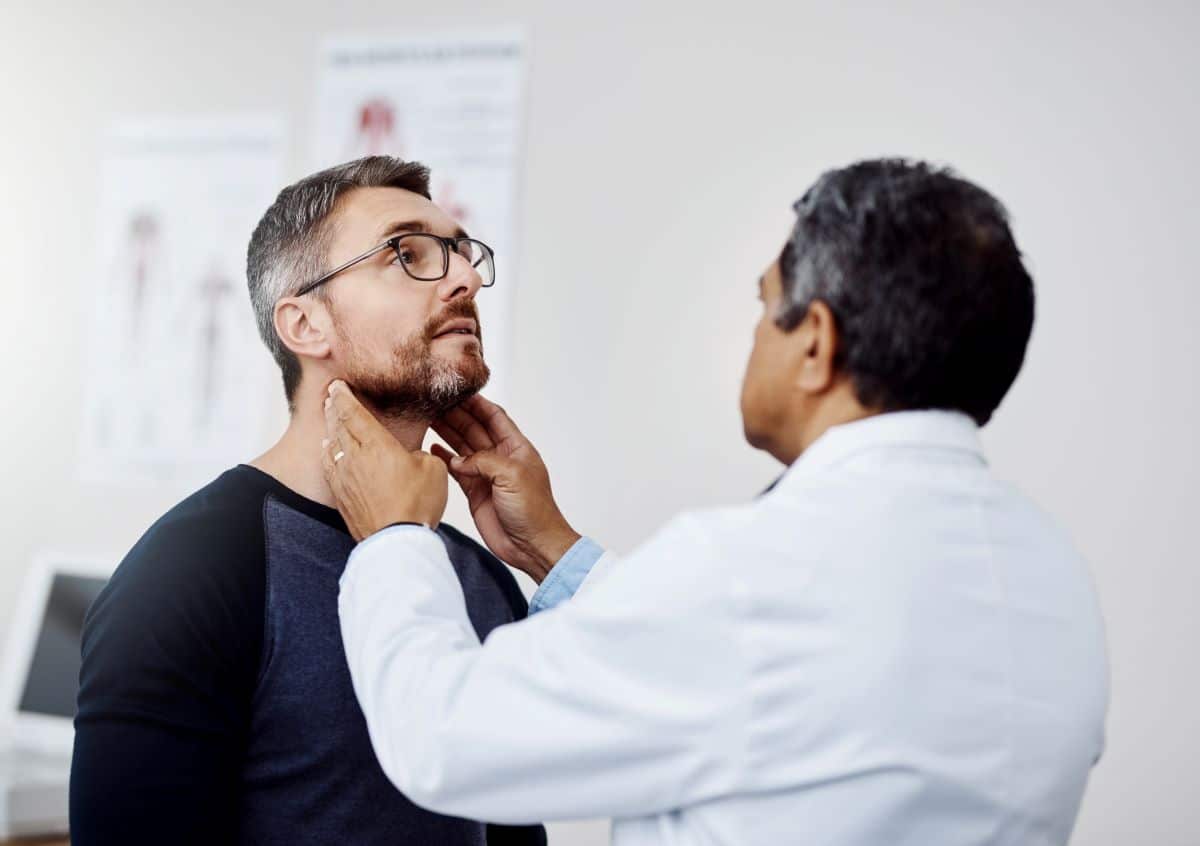 head-and-neck-cancer-evaluation Doctor feeling the throat of a patient in a clinical setting.