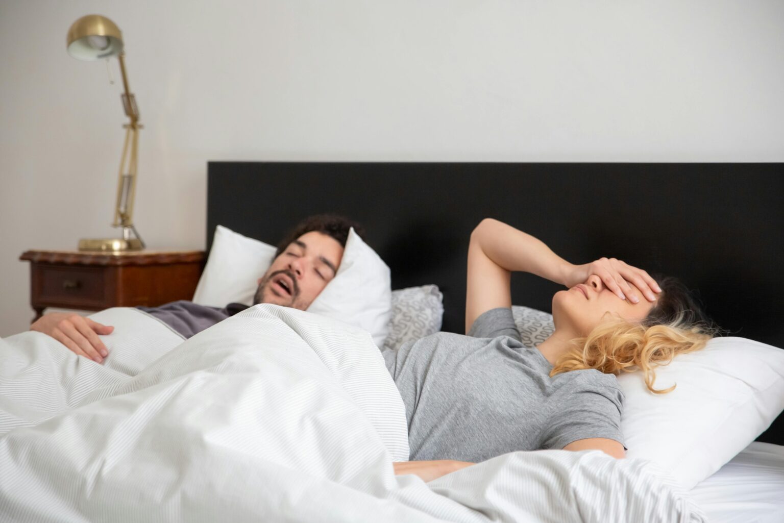 Couple with sleep apnea trying to sleep; one of them snores loudly and the other struggles to sleep