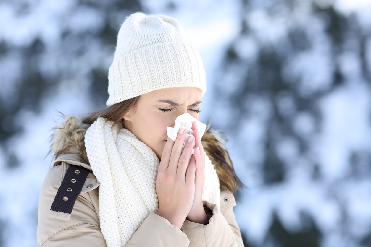 Woman bundled up for cold weather blowing her nose and experiencing congestion.